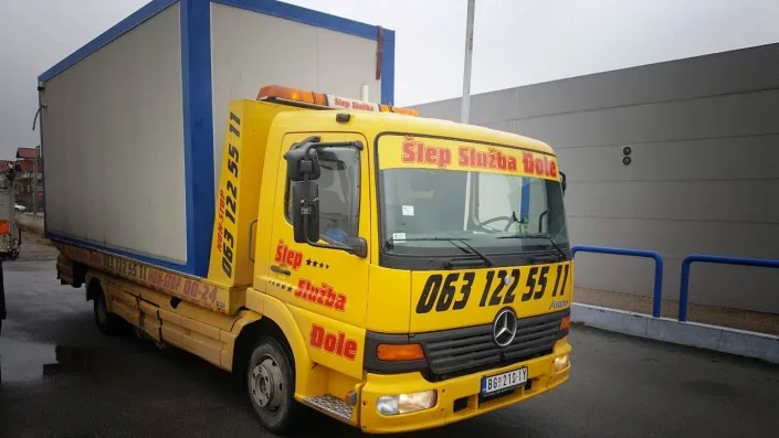 žuti šlep kamion vrši transport tereta - beli kontenjer sa plavim ivicama